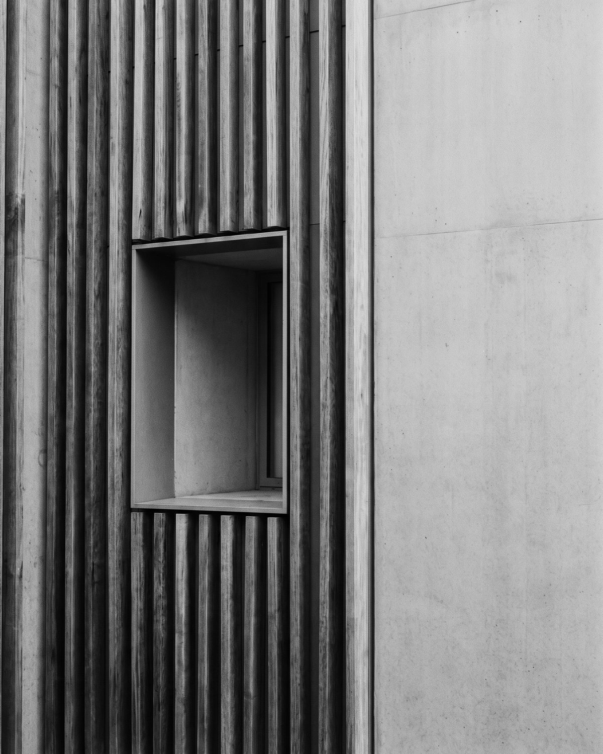 Timber slats meeting a concrete facade with one deep-set window.