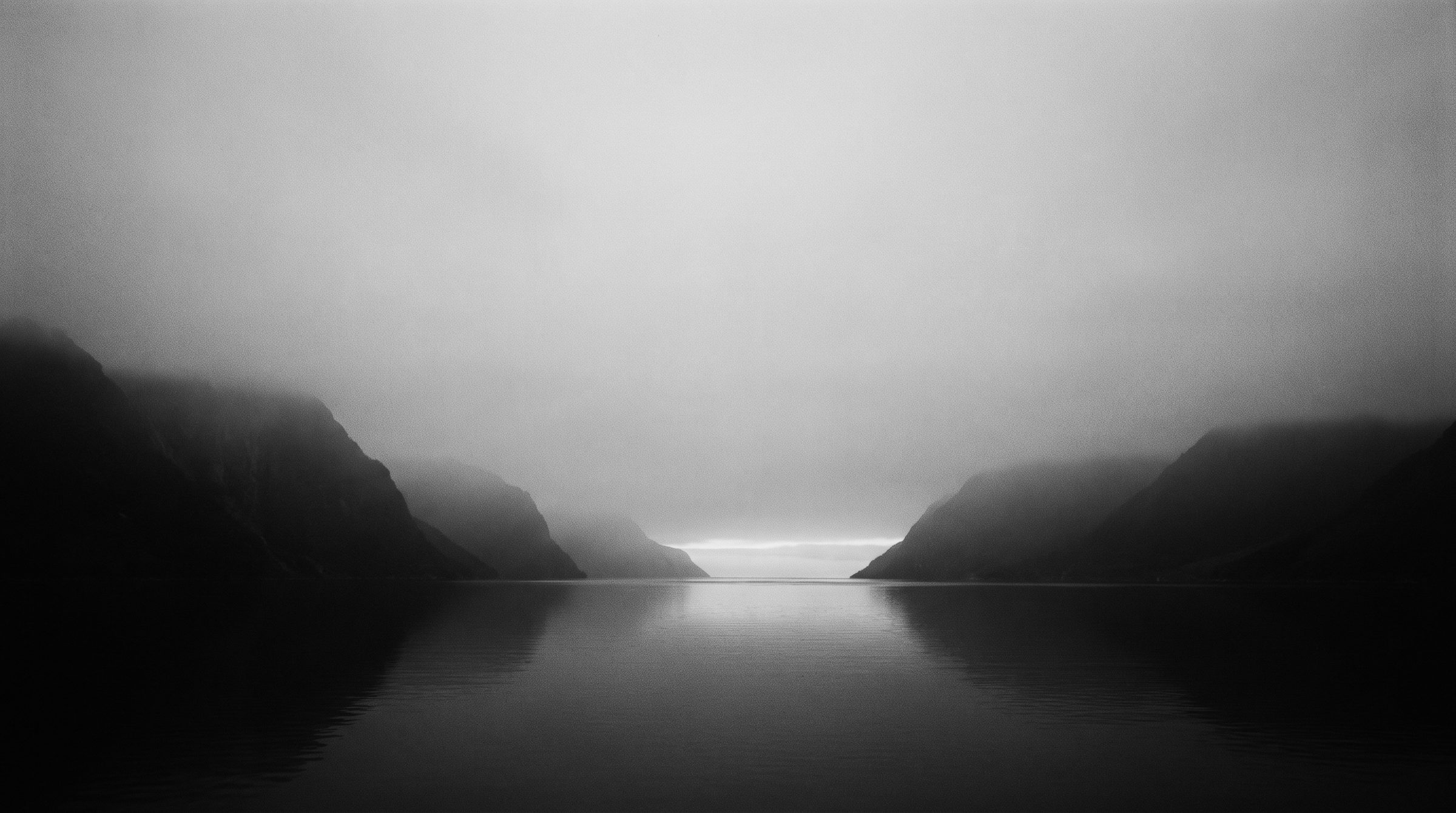 A still Norwegian fjord at dawn, mountains fading into mist.
