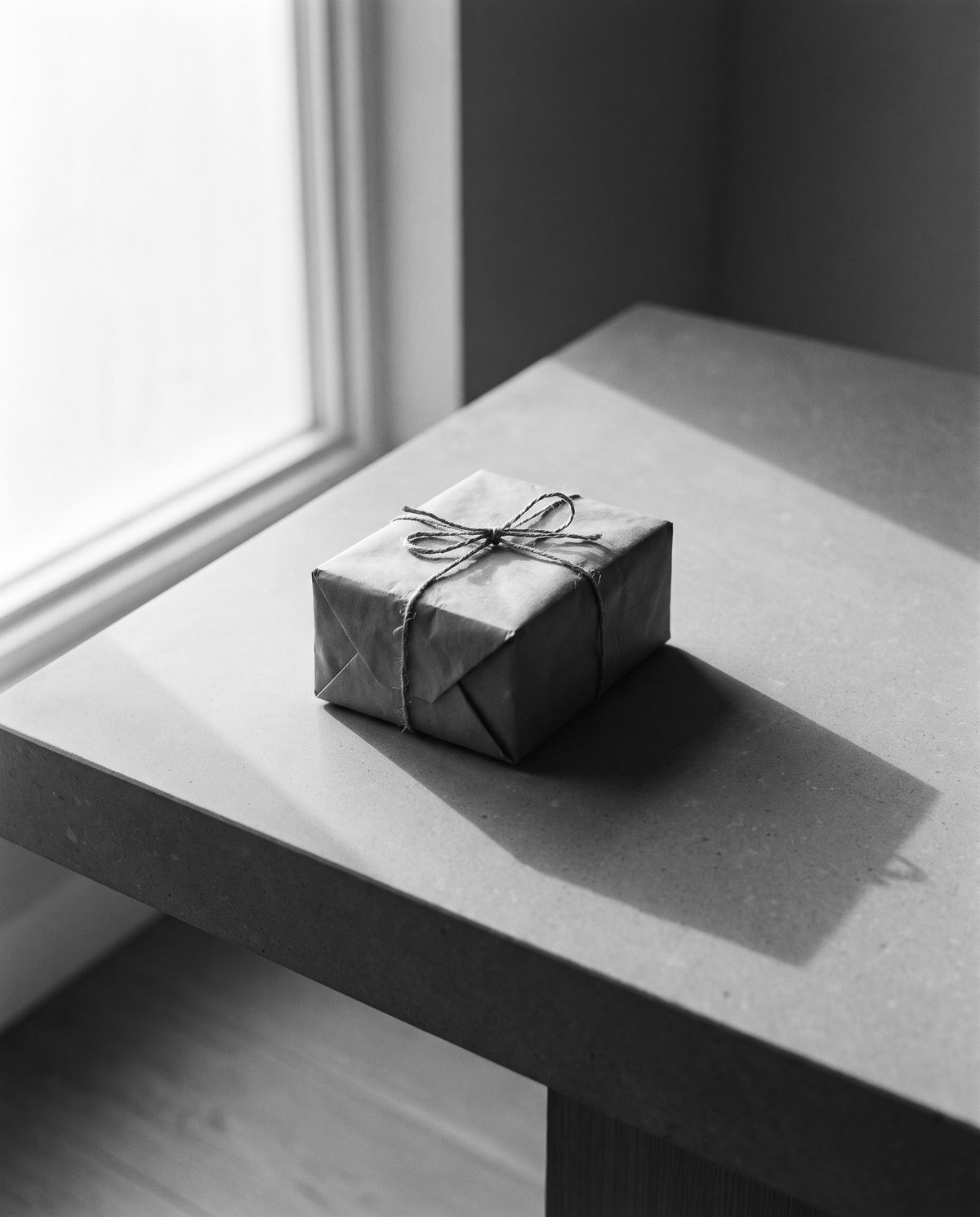 A plain brown-paper parcel tied with twine on a stone table by a window.